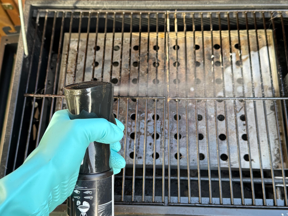 Eine Person sprüht im Test den Weber-Grillreiniger auf einen Grillrost.