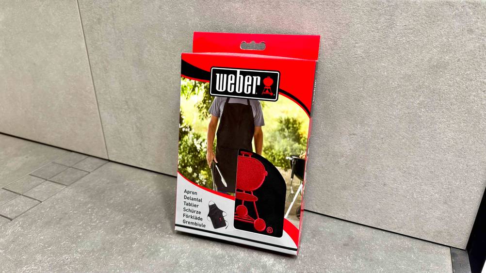 Eine getestete Grillschürze in der Verpackung lehnt an einer Steinplatte.