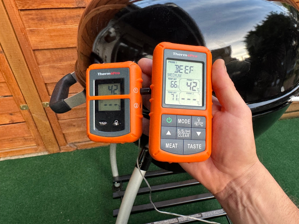 Eine Person hält vor einem Grill den Empfänger und den Sender des getesteten Grillthermometers von ThermoPro in der Hand.
