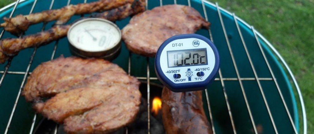 Ein Grillthermometer steckt in einem Stück Fleisch auf einem Grill