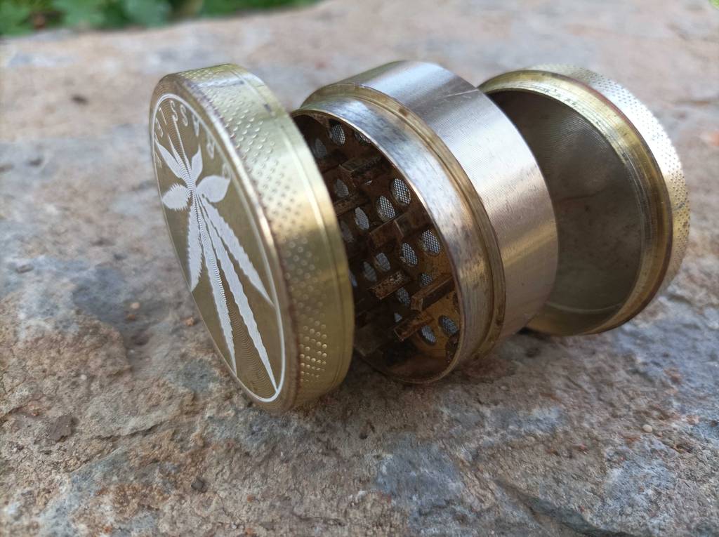 Ein getesteter Grinder liegt seitlich in Einzelteilen auf einer Steinfläche.