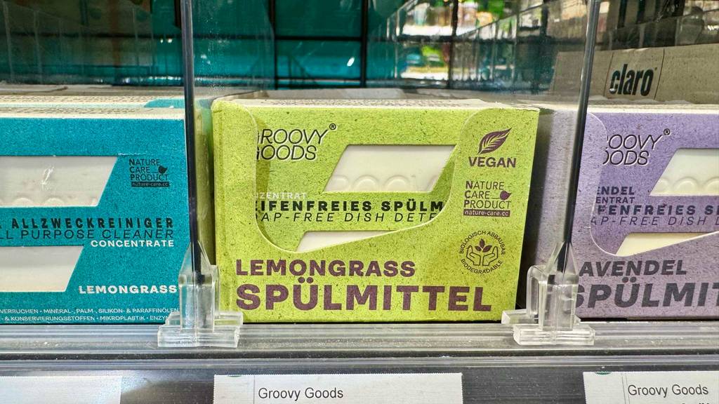 In einer grünen Verpackung befindet sich ein seifenfreies, festes Spülmittel im Test neben weiteren festen Reinigern in einem Verkaufsregal.