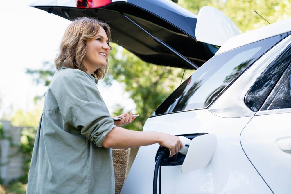 Growatt-Wechselrichter im Test: Eine Frau hält den Stecker eines Ladegeräts, der gerade in ihrem E-Auto steckt.