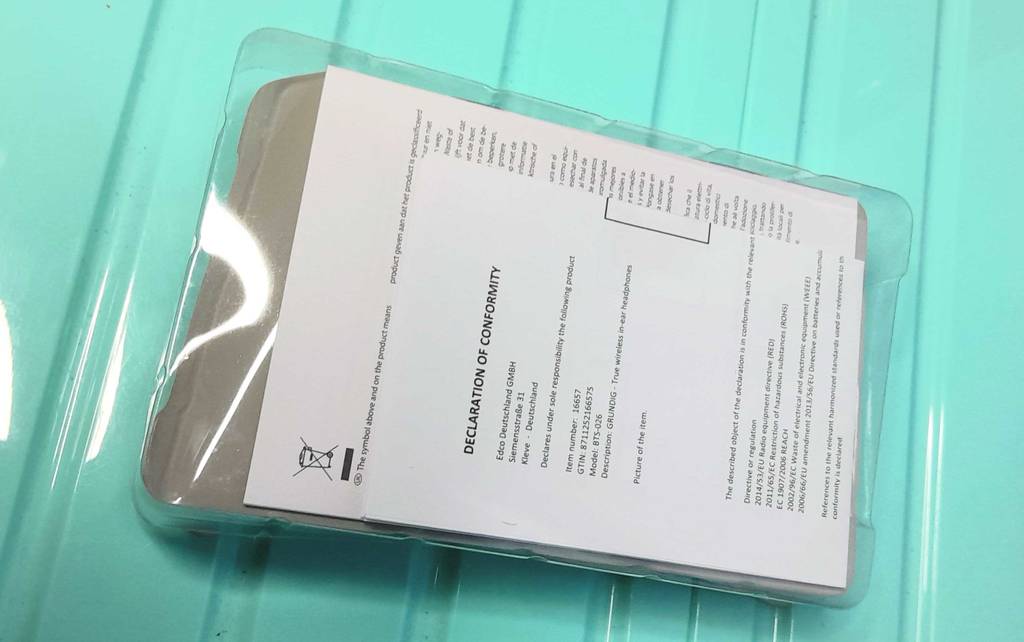 Declaration of Conformity in der auf türkisfarbiger Fläche liegenden Verpackung eines versandten Kopfhörers mit In-Ear Noise Cancelling im Test.