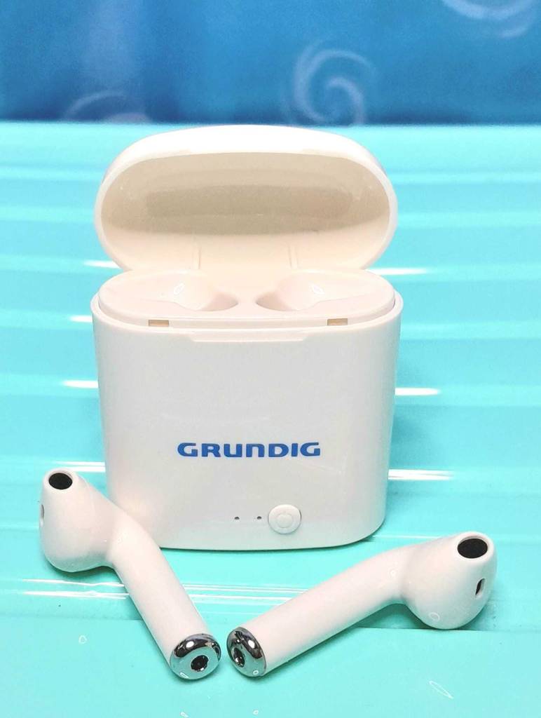 Kopfhörer mit In-Ear Noise Cancelling im Test: Gesamtansicht des Grundig True Wireless In-Ear-Kopfhörers inklusive Ladestation vor türkisfarbener Fläche.