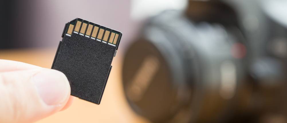 Eine Speicherkarte für eine GSM-Überwachungskamera wird vor eine Kamera gehalten. 