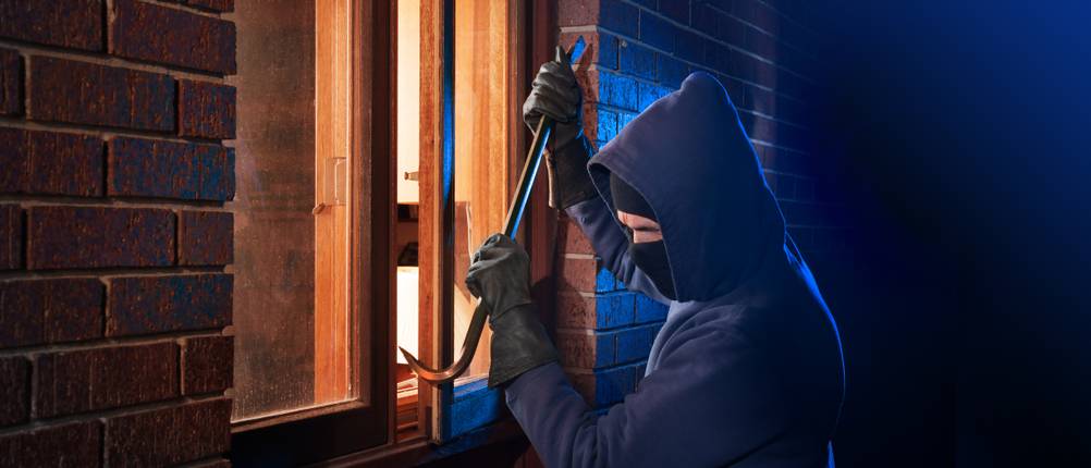 Ein Einbrecher versucht von außen das Fenster eines Hauses aufzuhebeln.