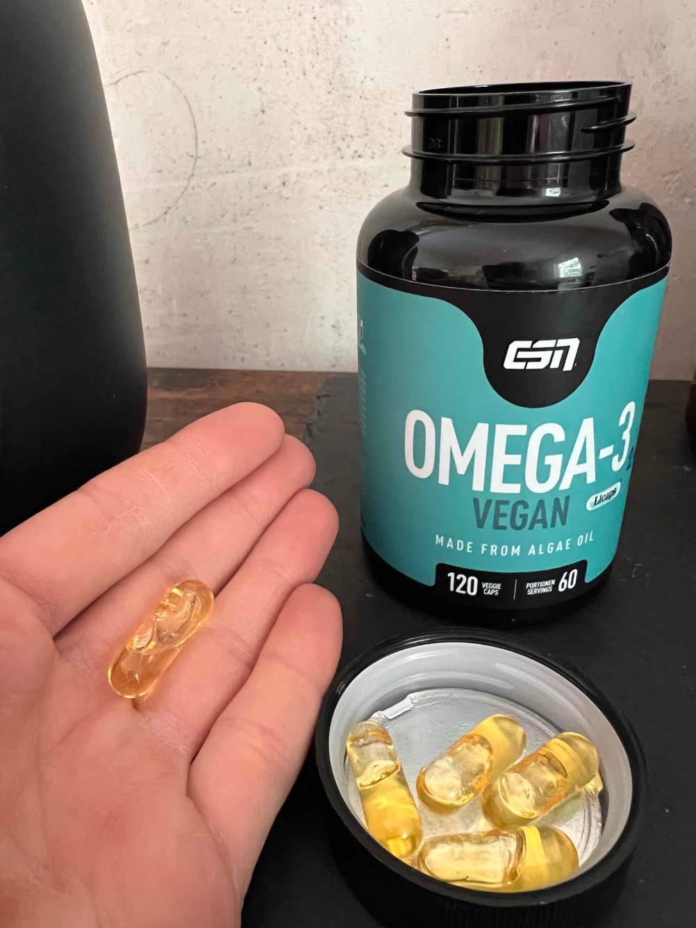 Nahrungsergänzungsmittel für Veganer getestet: Mehrere Kapseln Omega-3 liegen im geöffneten Deckel vor der Flasche, in einer Hand liegt eine Kapsel.