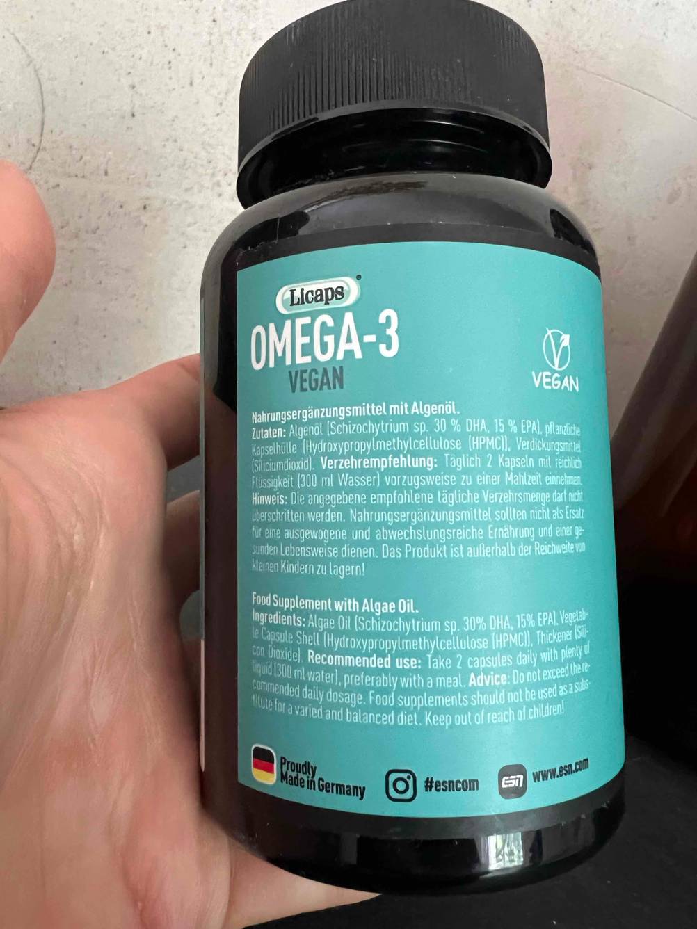 Hand zeigt die Rückseite einer getesteten Flasche Nahrungsergänzungsmittel für Veganer mit Angaben zu Inhalt und Verzehr.