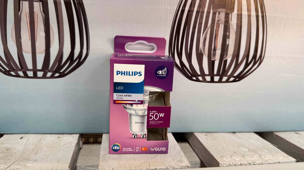 Vor einem Plakat auf Holz steht eine verpackte GU10-LED kaltweiß im Test.