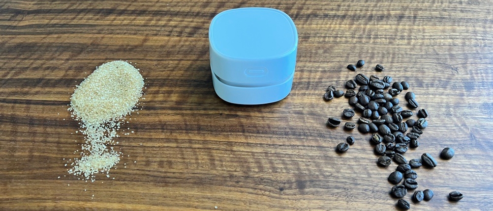 Zucker, Kaffeebohnen und das Gerät Gudoqi-Tischstaubsauger CE2382 auf einem Tisch.