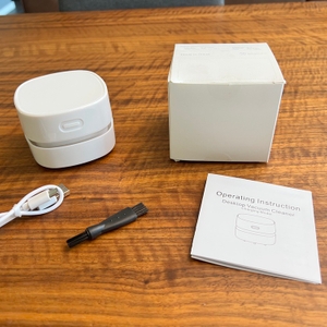 Tischreiniger, Karton, Anleitung, Kabel und Reinigungsbürste auf einem Tisch.