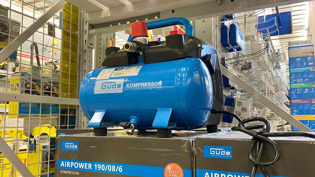 Ein blau-schwarzer Güde Kompressor im Test steht auf seiner Originalverpackung in einem Baumarkt.