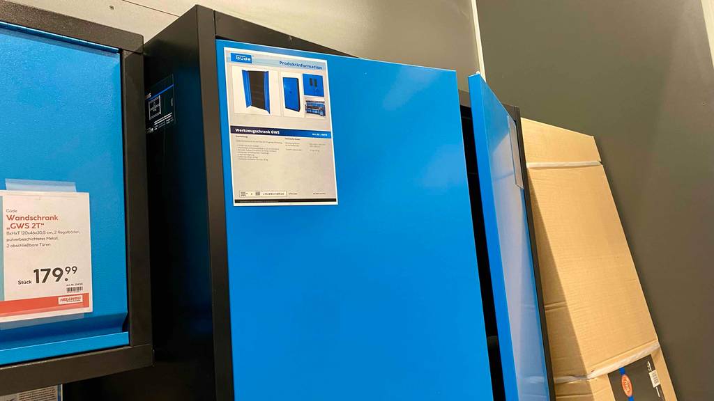 Werkzeugschrank im Test: Auf einer leicht geöffneten Tür eines blauen Schranks ist ein Produktinformationsblatt angebracht.