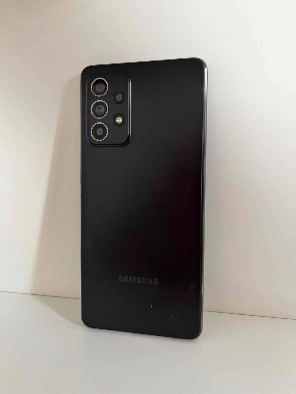 Günstiges Smartphone getestet: Ein Gerät von hinten mit Logo und Kameras an einer hellen Wand lehnend.