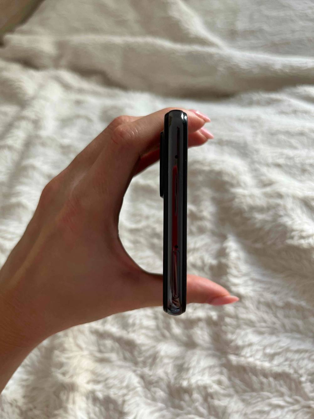 Eine Hand hält ein getestetes günstiges Smartphone mit der Kopfseite nach oben vor eine helle Fläche.