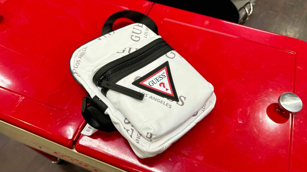 Brustbeutel im Test: Ein weißes Modell von Guess liegt auf einer roten Oberfläche.