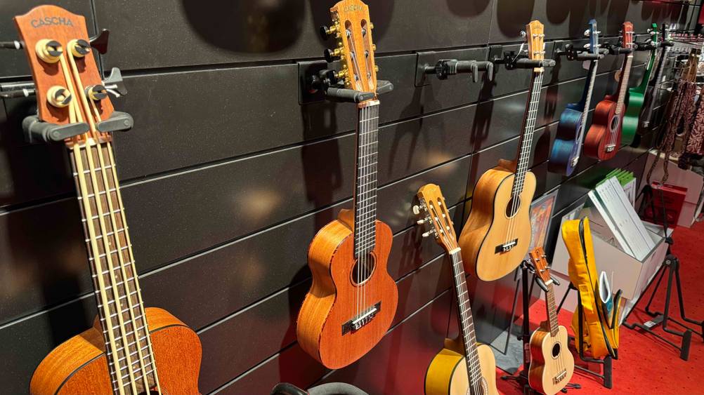 Getestet: Eine Guitarlele von der Seite mit mehreren anderen Insturumenten an einer Wand hängend.