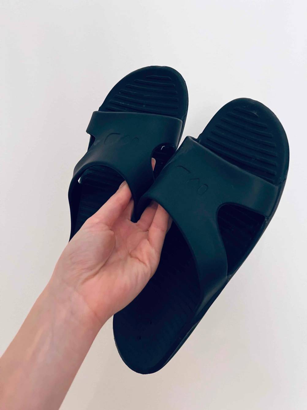 Eine Hand hält schwarze, getestete Herren-Pantoletten aus Gummi vor einem weißen Hintergrund.