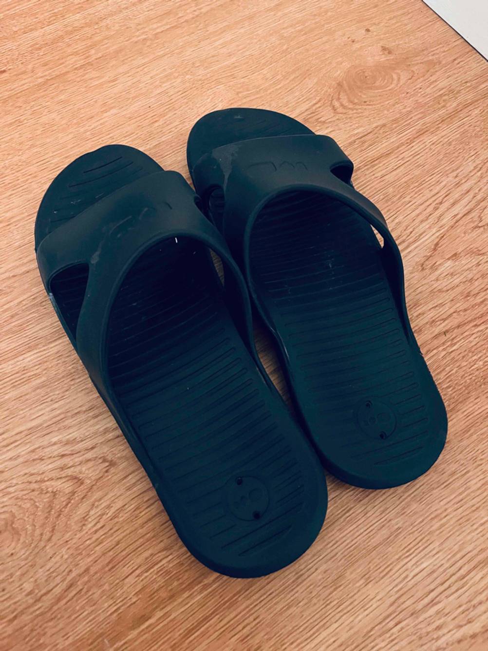 Ein Paar schwarze Herren-Pantoletten im Test steht auf einer Holzoberfläche.