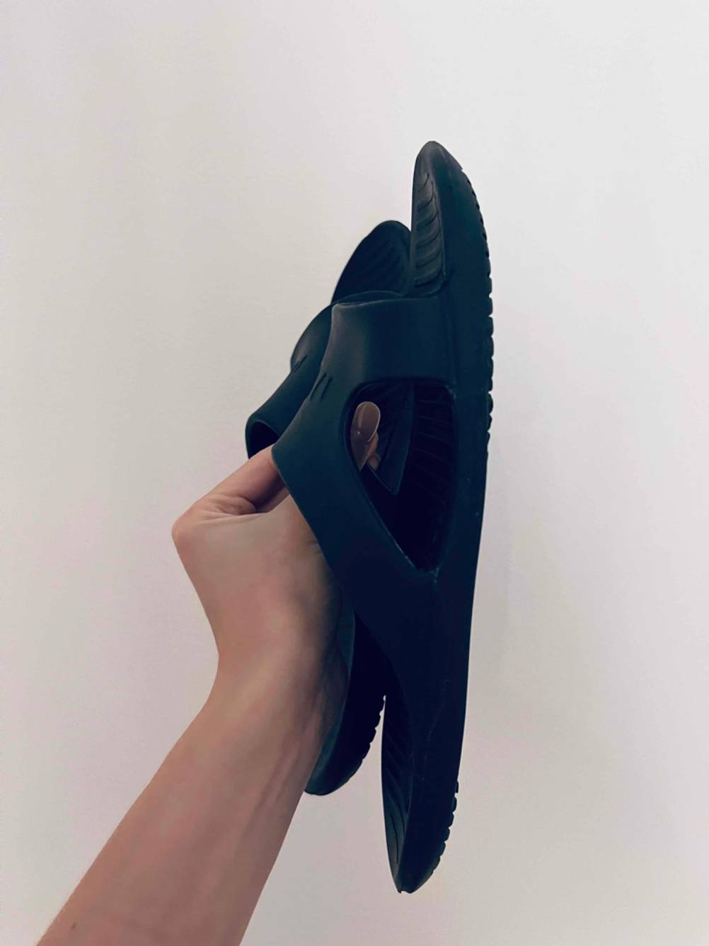 Schwarze Gummi-Pantoletten für Herren im Test werden von einer Hand vor hellem Hintergrund hochgehalten.