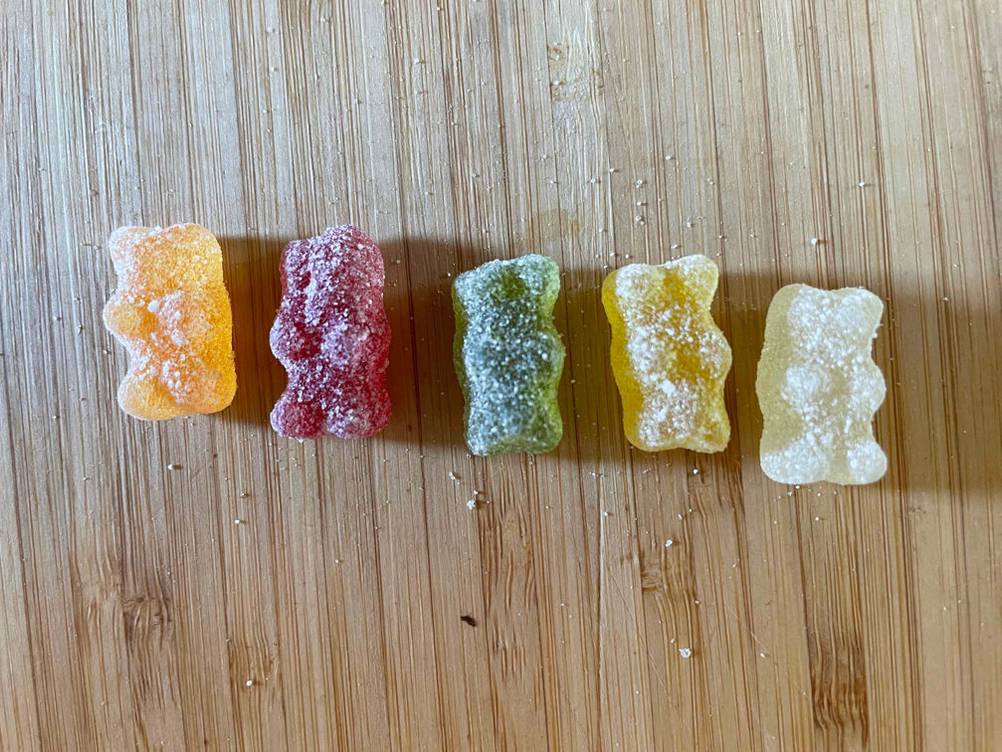 Im Test: Mehrere verschiedenfarbige Gummibärchen aufgereiht auf einer Holzfläche.