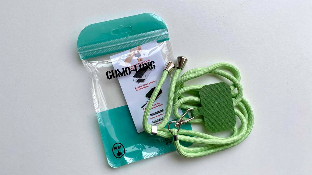 Eine grüne Handykette im Test liegt auf seiner transparenten Kunststofftüte inklusive Anwendungsinformationen auf einer weißen Fläche.