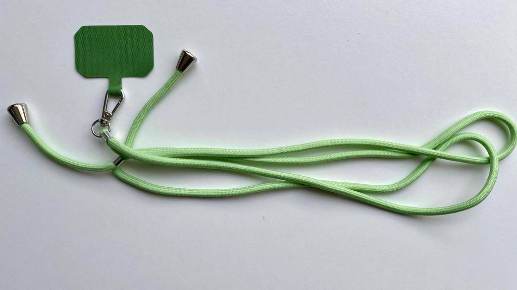 Eine grüne, verlängerbare, getestete Handykette liegt auf weißem Untergrund.