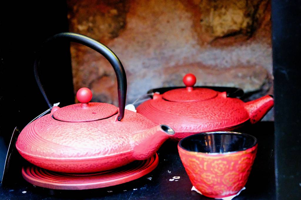 Gusseiserne-Teekanne-Test: Zwei rote Teekannen aus Gusseisen stehen auf einem Tisch. Daneben befindet sich ein kleines rotes Teeglas. 