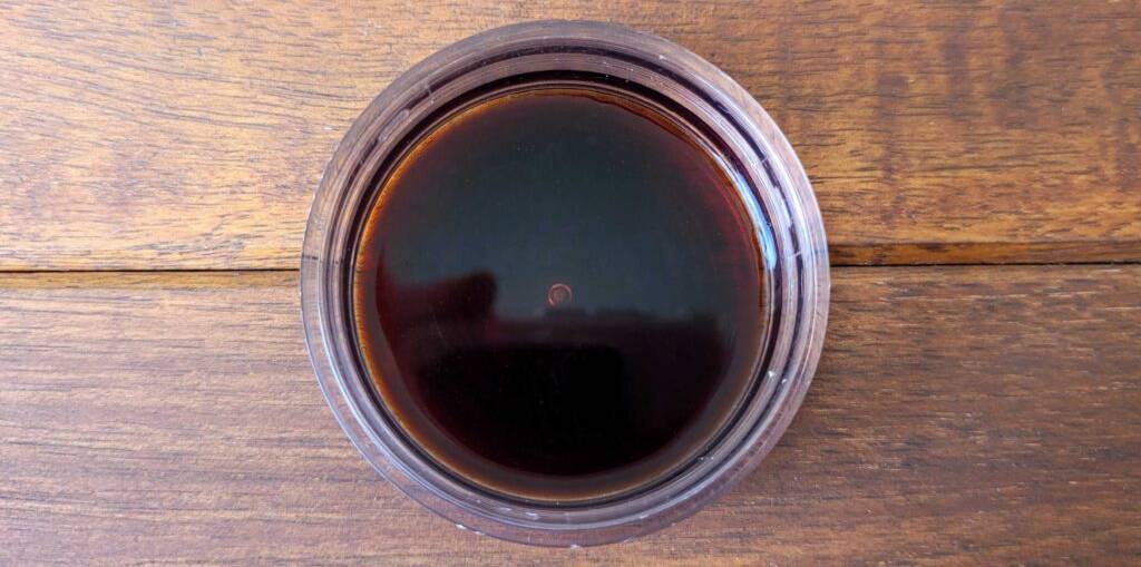 Balsamico-Essig im Test: Eine braune Flüssigkeit von oben betrachtet, befindet sich in einem Messglas auf einer Holzoberfläche.