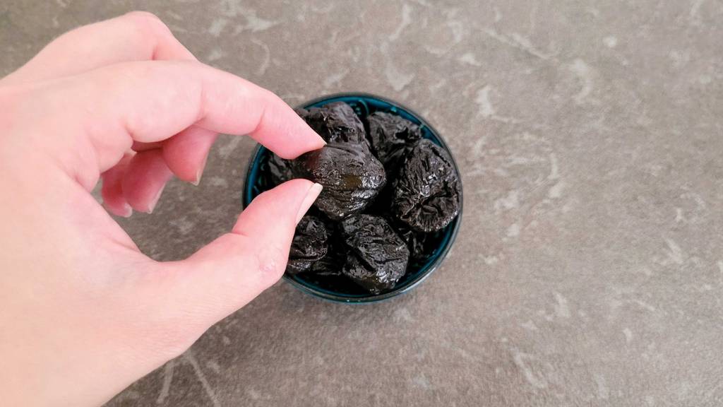 Trockenpflaumen im Test: Eine Hand pickt eine Pflaume aus einer Schale.