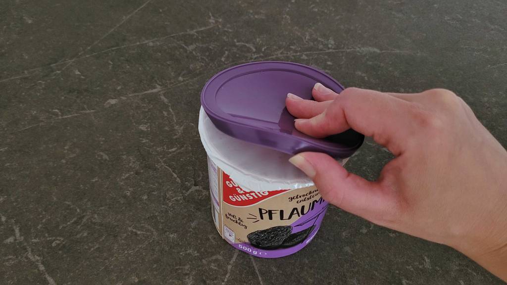 Eine Hand öffnet den Plastikdeckel einer Packung Trockenpflaumen zum testen.