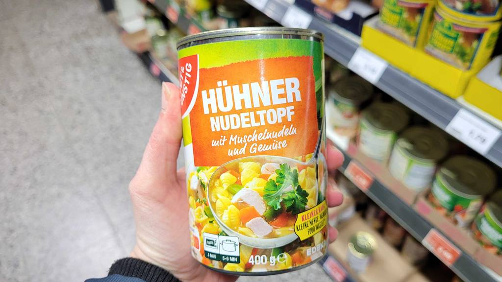 Eine Hand hält eine Dose mit Hühnersuppe im Test vor einem Verkaufsregal.