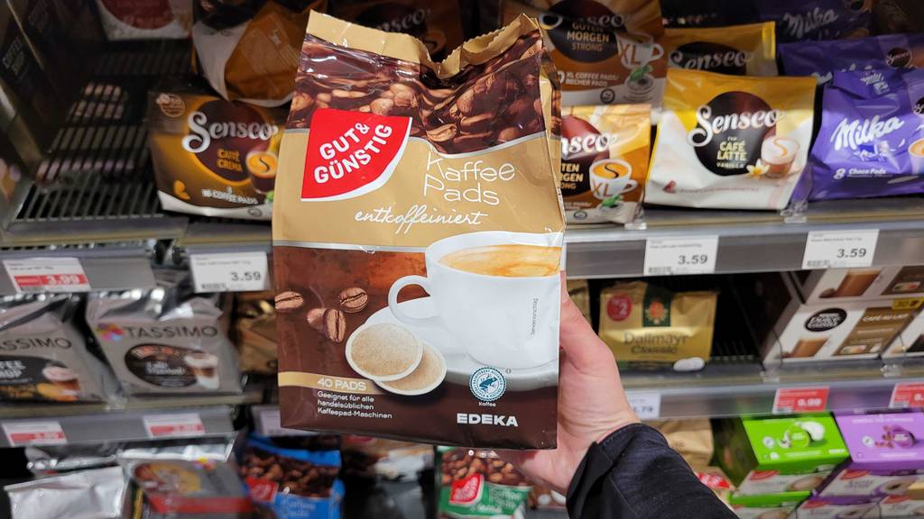 Im Test: Eine Hand hält eine Packung Kaffeepads entkoffeiniert vor einem Verkaufsregal.
