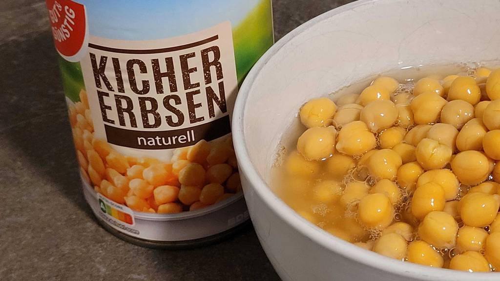Getestete Kichererbsen aus der Dose befinden sich in einer weißen Schüssel, die neben der Dose steht.