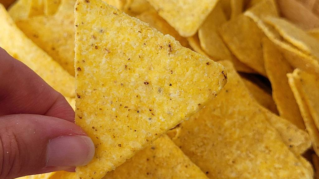 Nahaufnahme zweier Finger, die einen getesteten Tortilla-Chip halten.