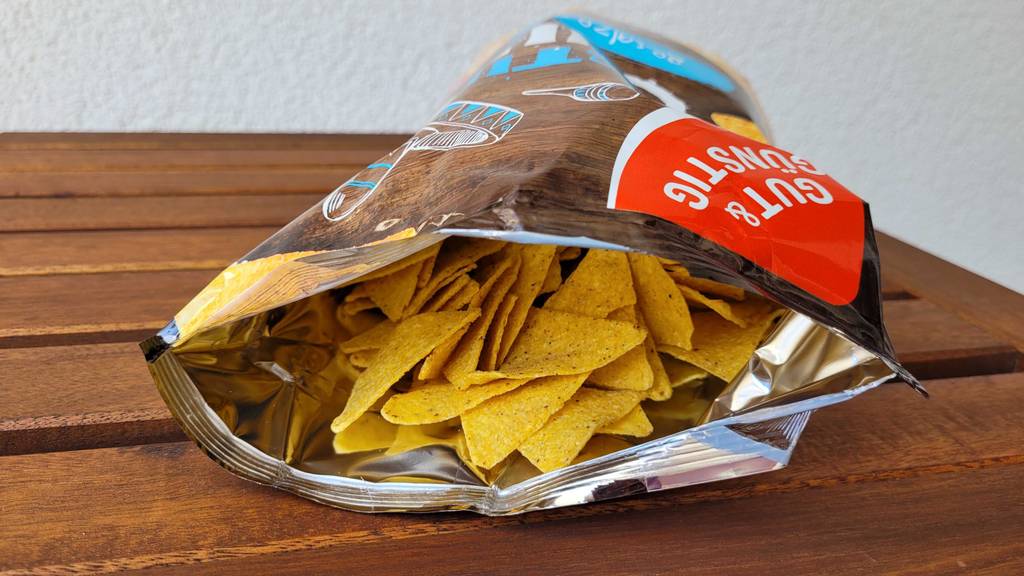 Getestete Tortilla-Chips liegen in ihrer Tüte auf einem Holztisch.