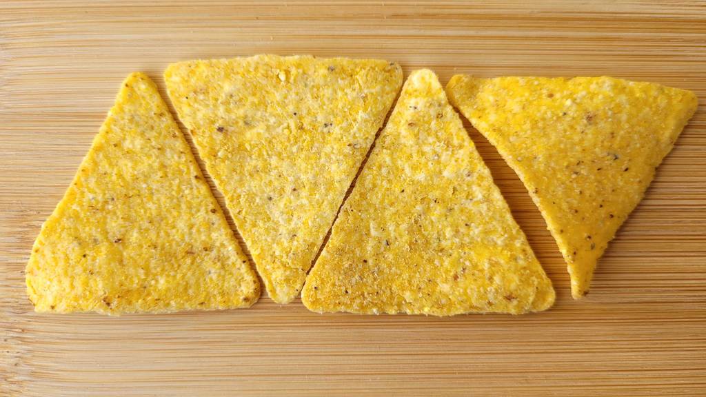 Aneinandergelegte dreieckige Tortilla-Chips im Test liegen auf einem Holzbrett.