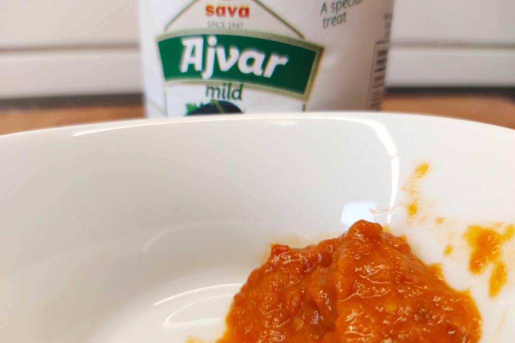 Im Test: Sava Ajvar in einer weißen Schale mit Glas im Hintergrund.