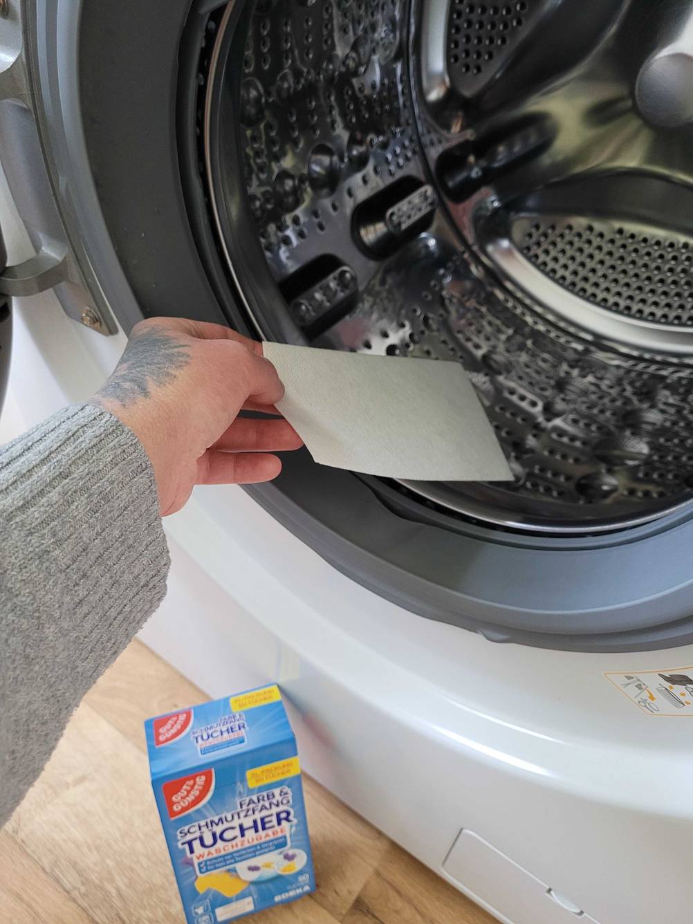 Im Test: Eine Hand gibt ein Farbfangtuch in eine Waschtrommel.