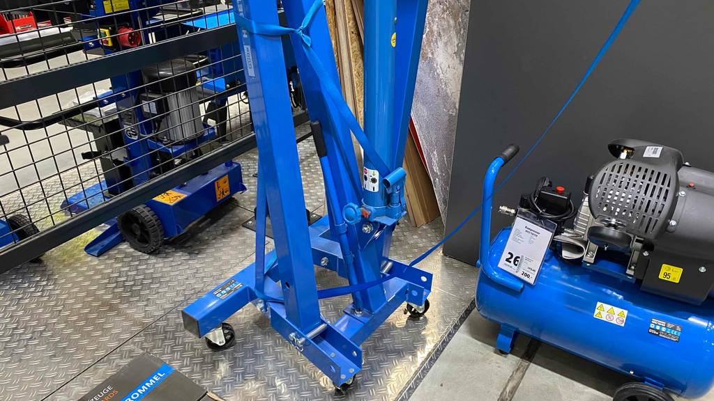 Detailansicht des zusammenklappbaren Gestells auf Rollen eines Werkstattkrans im Test, der in einem Verkaufsbereich steht.