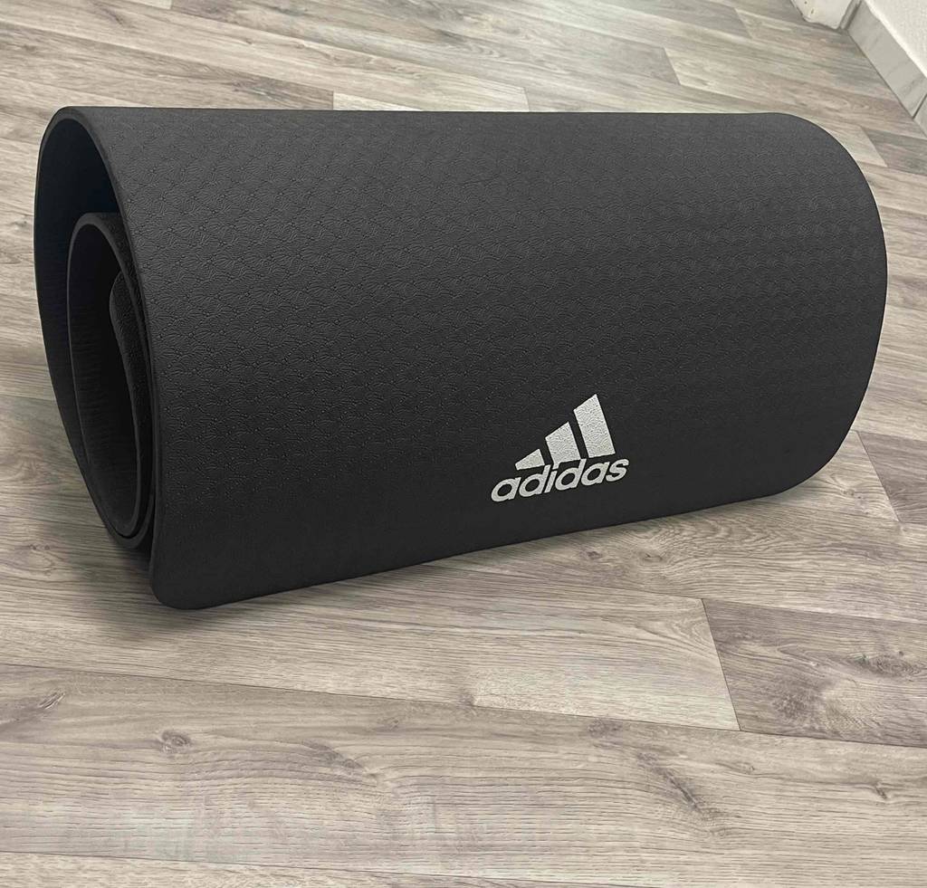 Eine getestete Gymnastikmatte in schwarz liegt zusammengerollt auf einem Laminatboden.