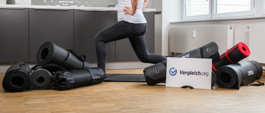 Zahlreiche Gymnastikmatten liegen auf dem Boden, eine Matte ausgebreitet, eine Frau macht eine Übung auf einer Matte.