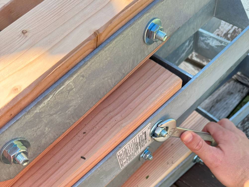 Ein H-Anker wird an mehreren Holzpfosten befestigt.