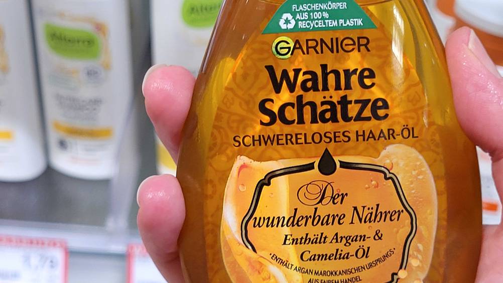 Haaröl getestet: Nahaufnahme des Logos und der Artikelbezeichnung auf einer Flasche die von einer Hand gehalten wird.