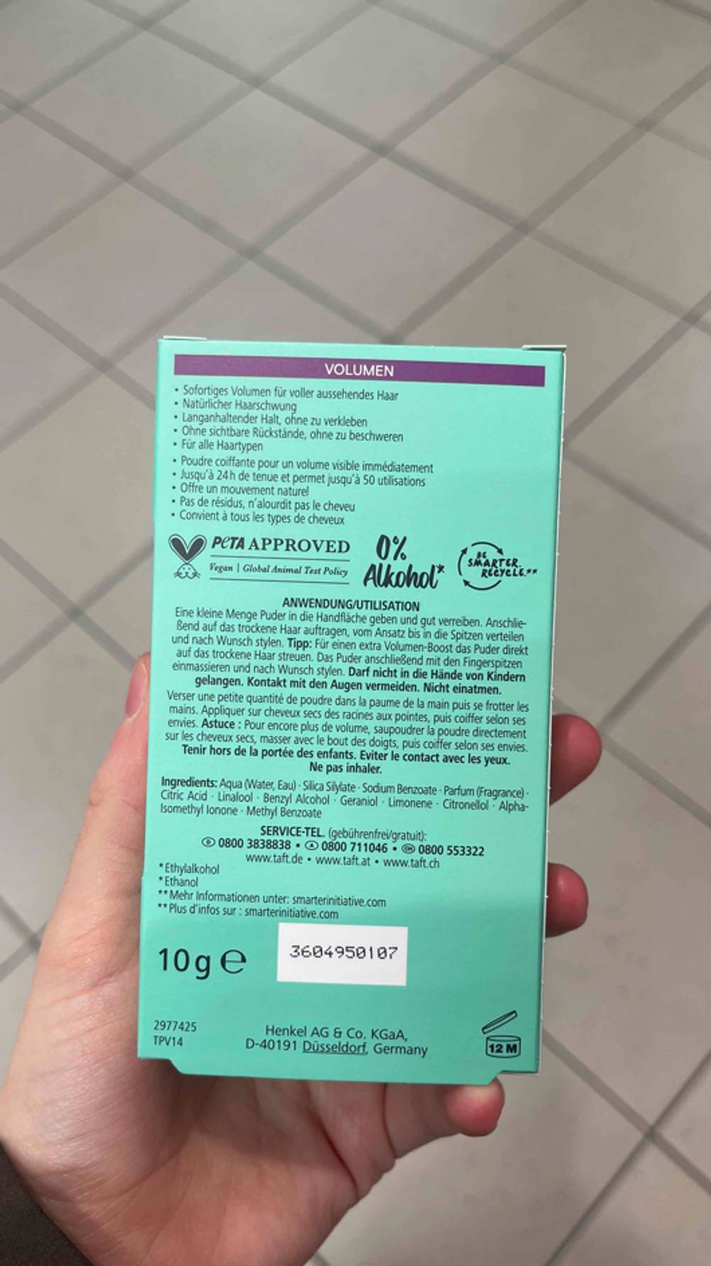 Das Haarpuder im Test befindet sich innerhalb der grünen 10-g-Verpackung die von einer Hand vor einem weißen Fliesenboden gehalten wird.