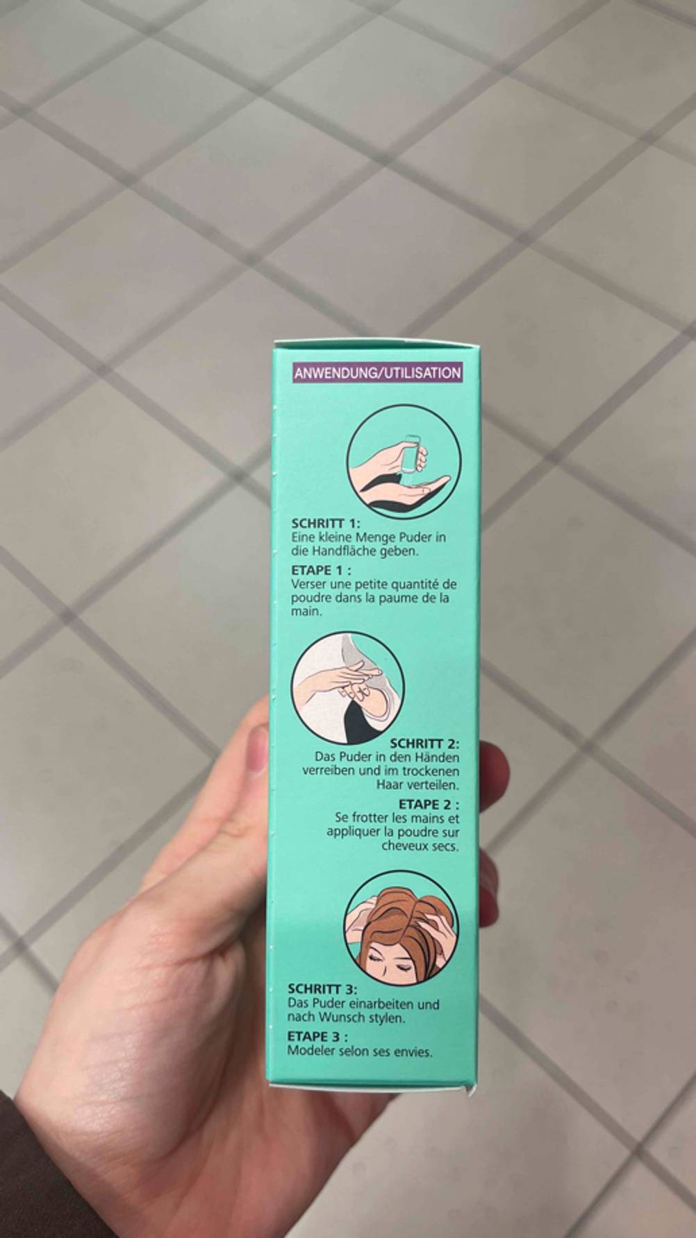 Das getestete Haarpuder in einer grünen Schachtel inklusive Anwendungsbeschreibung wird von einer Hand gehalten.