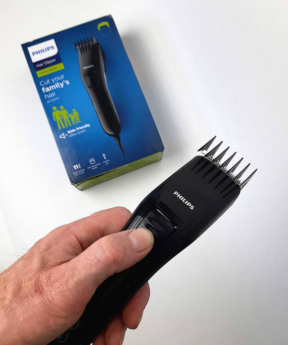 Eine Hand hält die getestete Haarschneidemaschine mit Kabel über die Originalverpackung.
