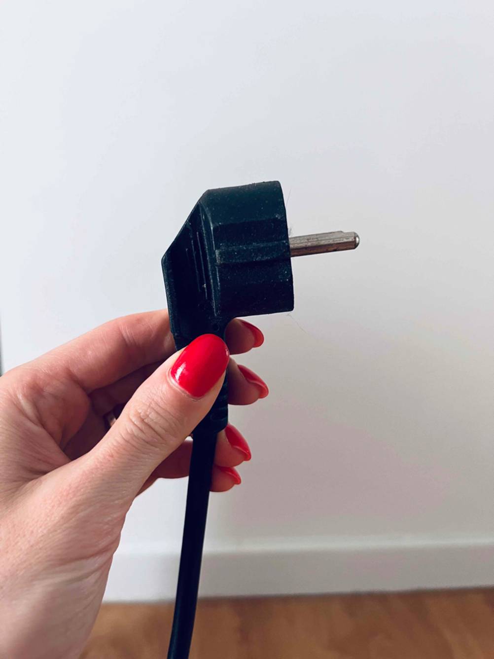 Getestete Heizung: Nahaufnahme einer Hand, die einen schwarzen Stecker vor hellem Hintergrund hält.