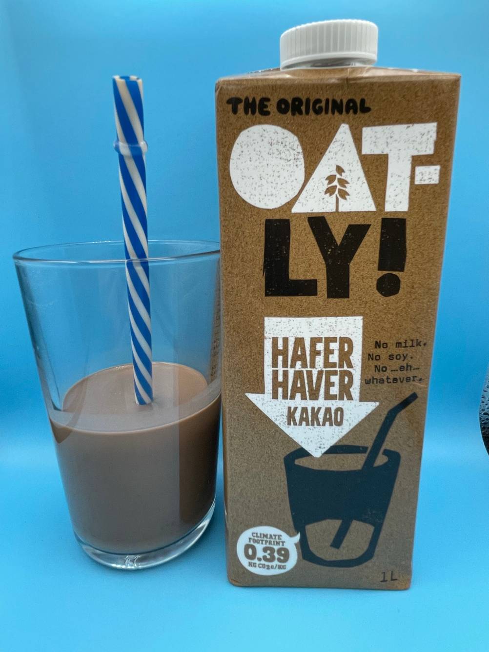 Ein Glas gefüllt mit getestetem Haferdrink befindet sich neben der Verpackung. 